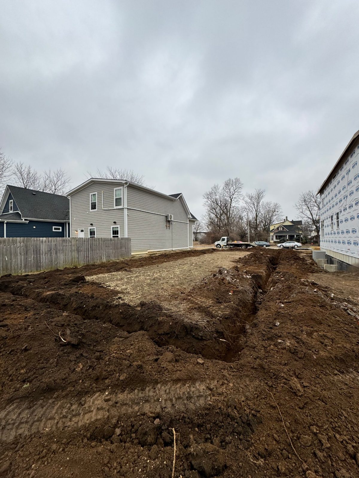 Excavated site with foundation trenches beside a completed home